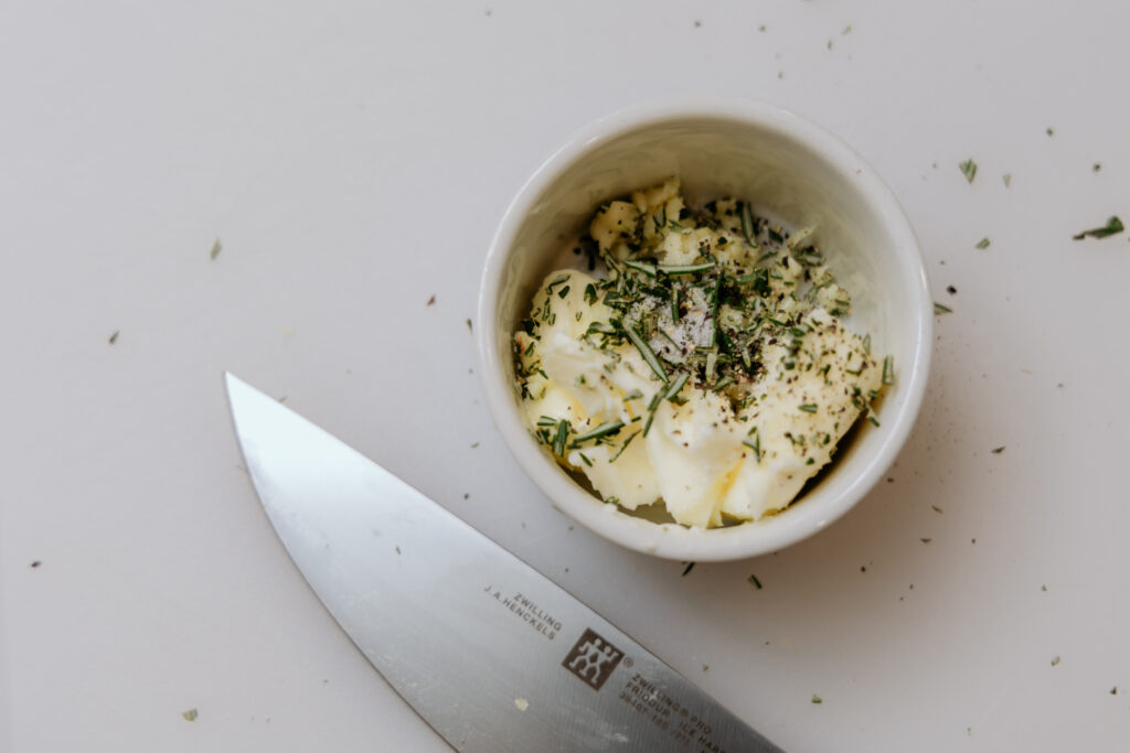 Ramekin filled with herb butter on cutting board.