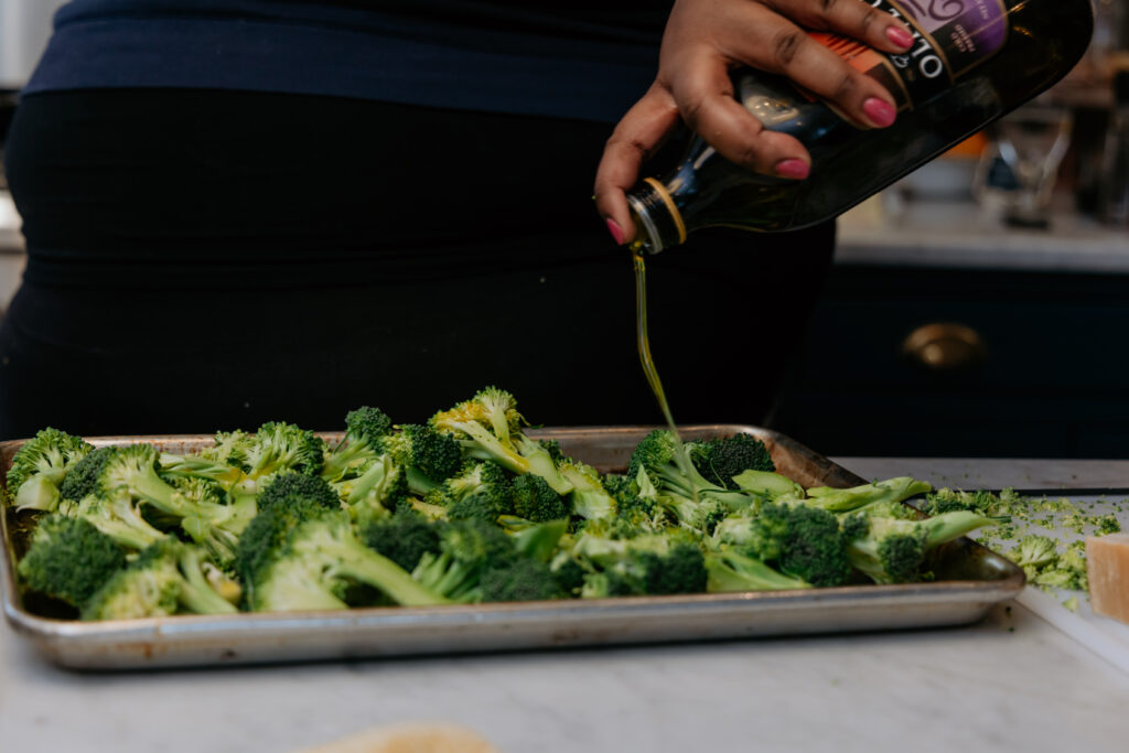 Kandice is drizzling olive oil over broccoli.