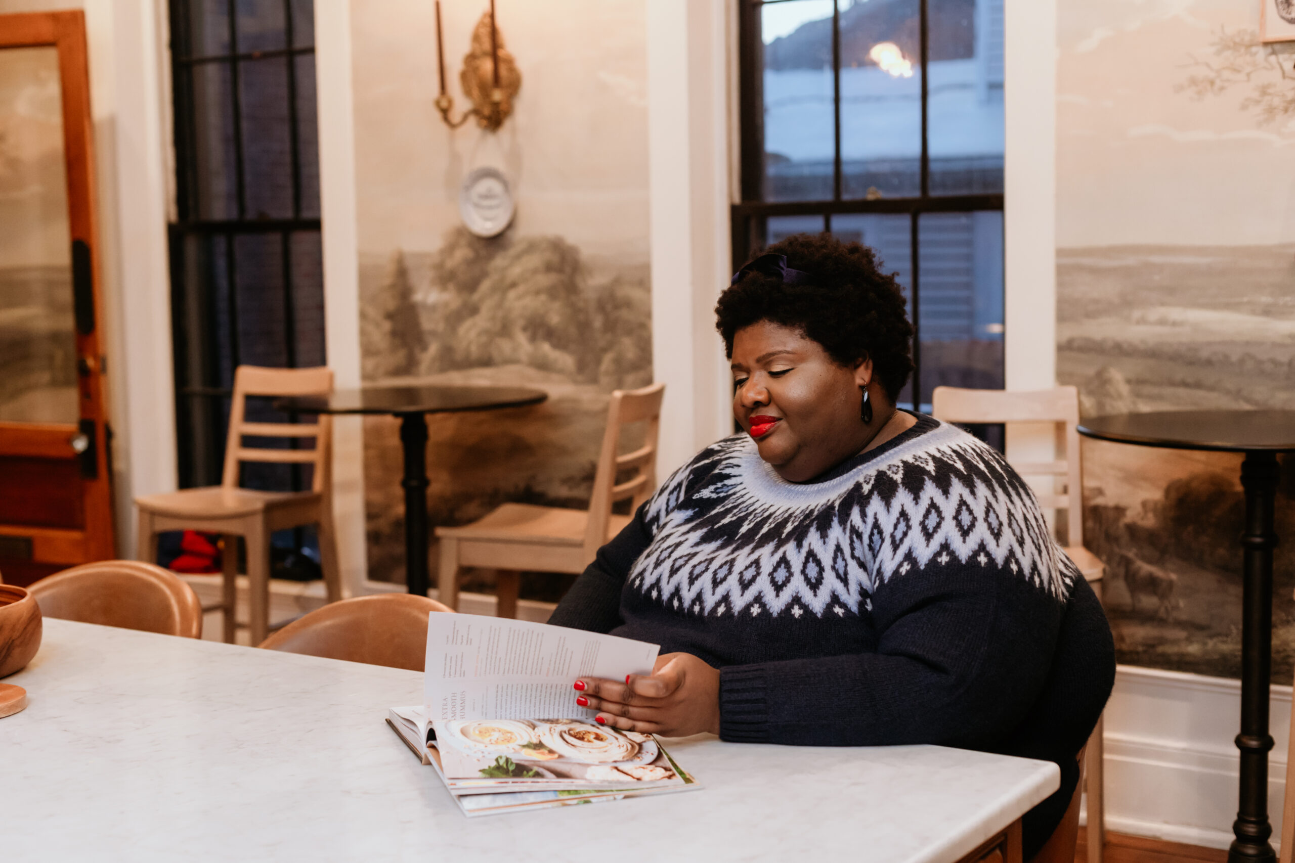 Kandice is siting at a kitchen corner, flipping thru a cookbook.