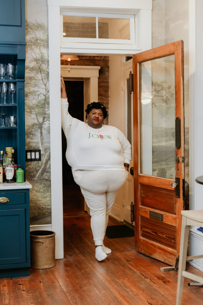 Kandice is standing in a doorway wearing all white.