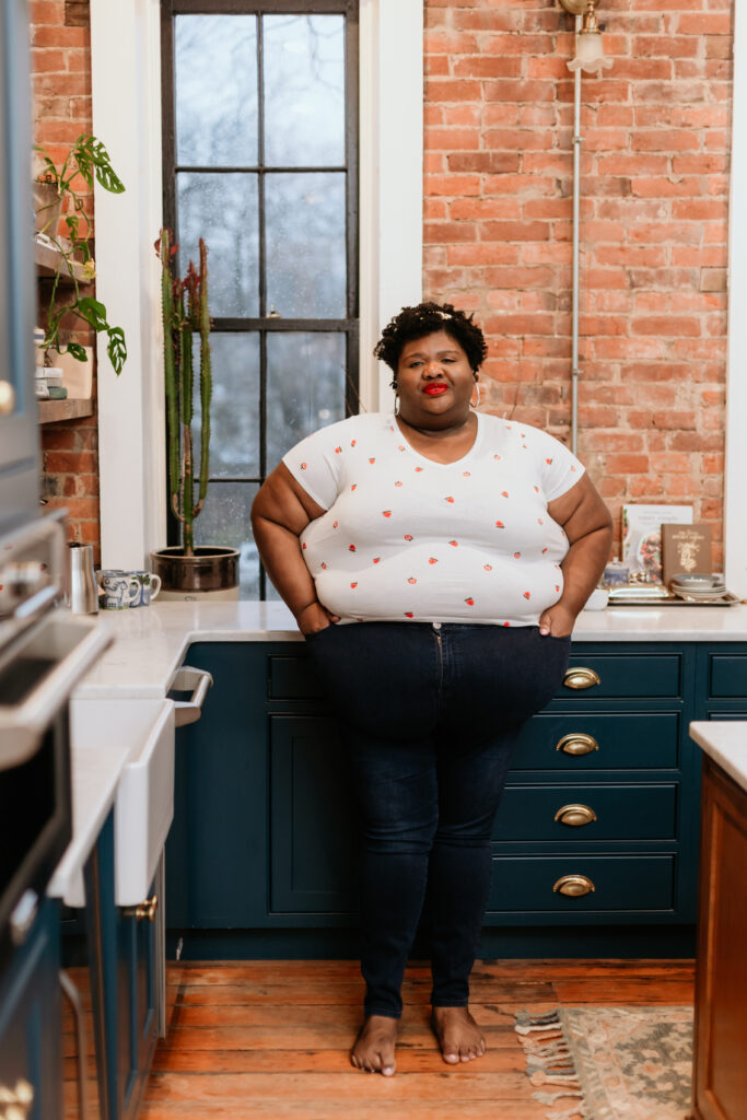 Kandice is standing in a kitchen in a strawberry tshirt.