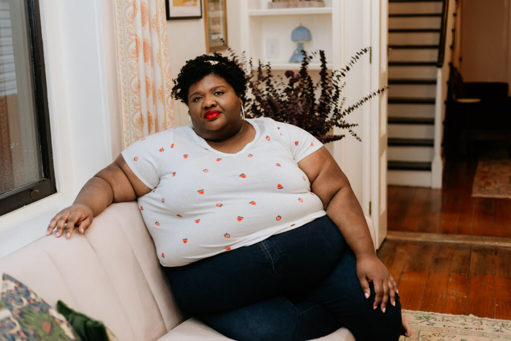 Kandice is sitting on a couch, wearing a fun strawberry t-shirt.