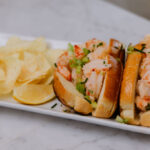 A shrimp roll sits on a platter with chips.