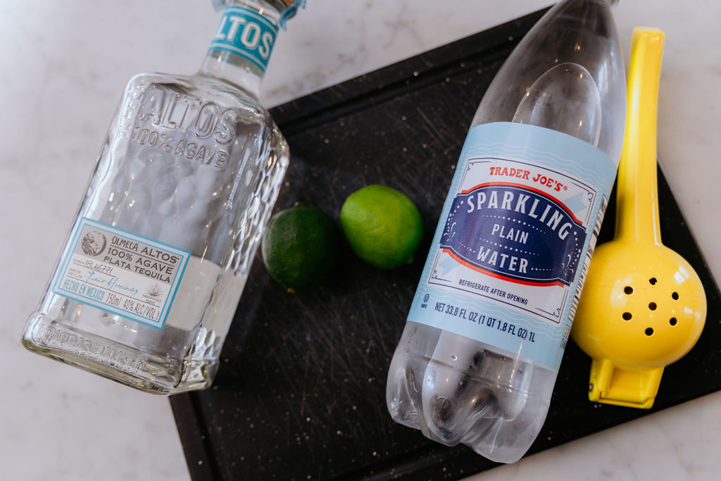 Tequila, limes, and sparkling water are displayed on a cutting board for texas ranch water