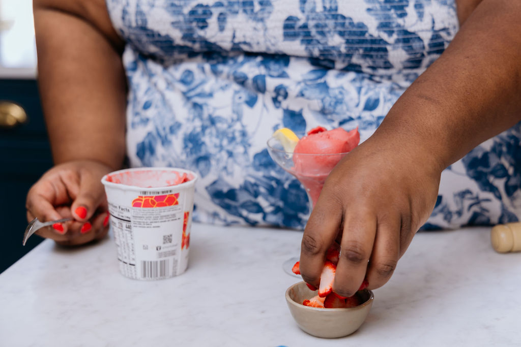 Kandice is sprinkling strawberries into glass.