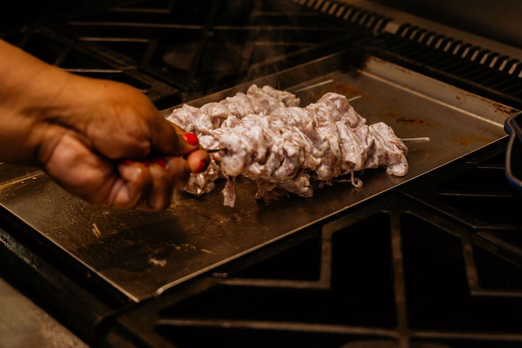 Kandice is placing chicken gyro skewers on hot grill.