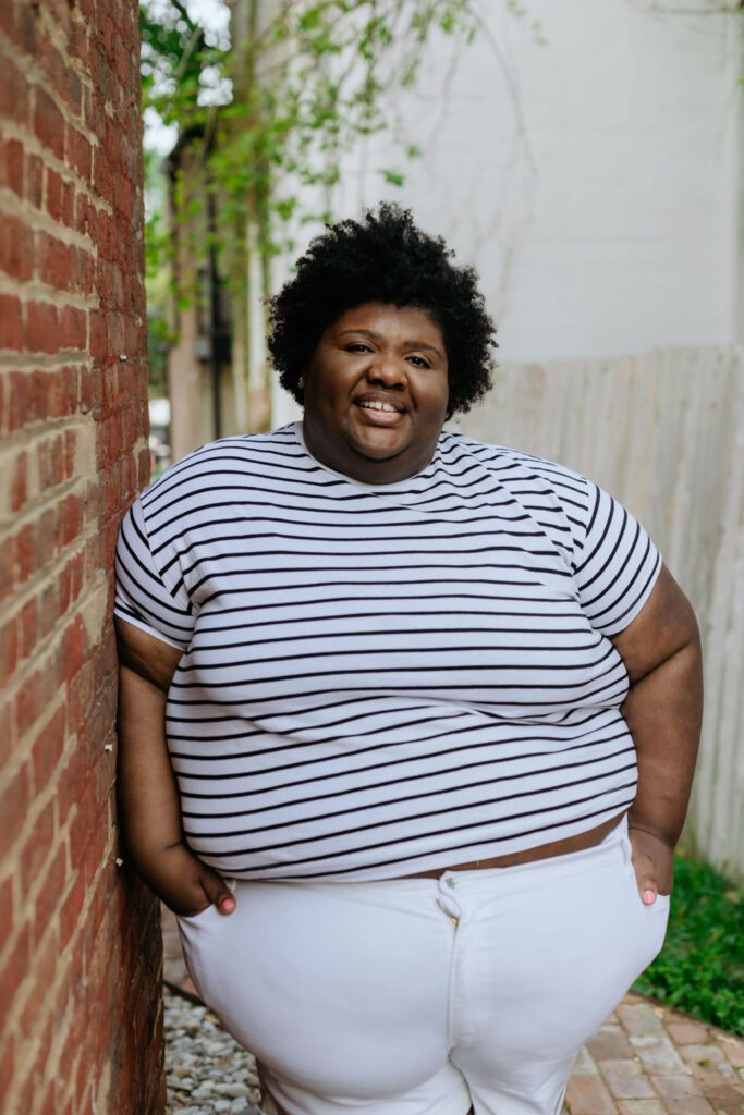 Kandice is leaning against a brick wall wearing a striped shirt showing how to style white shorts.