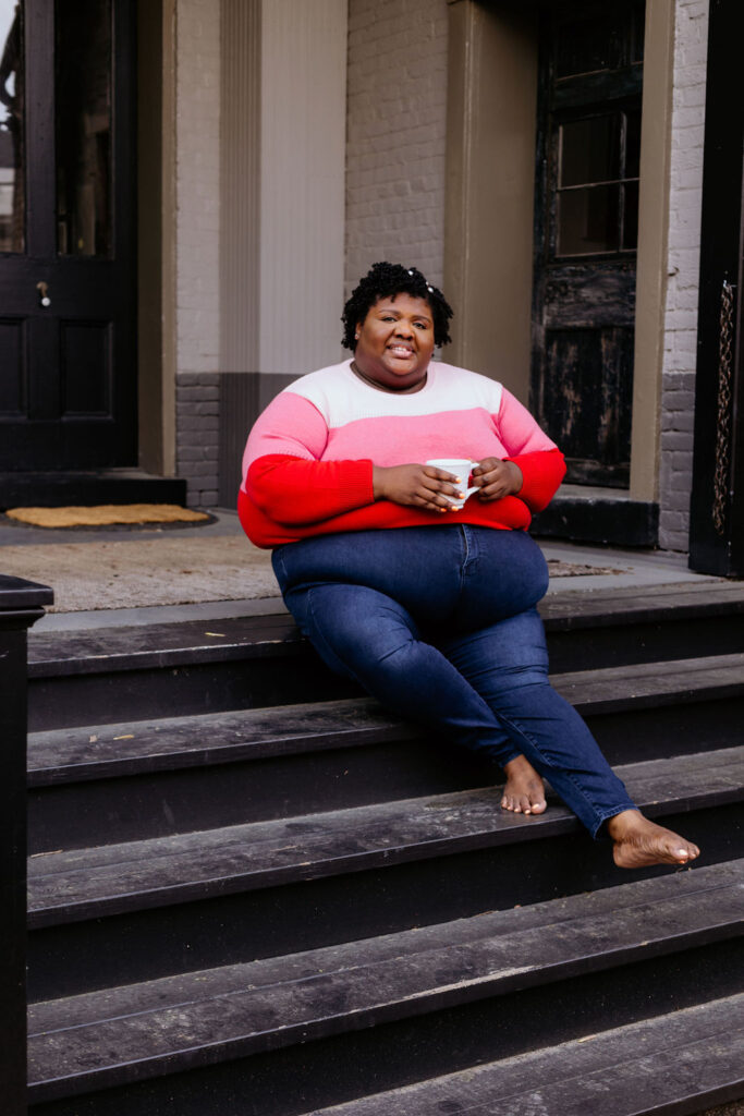 Kandice is sitting on porch steps, holding a mug. She is showing how to pose better in photos.