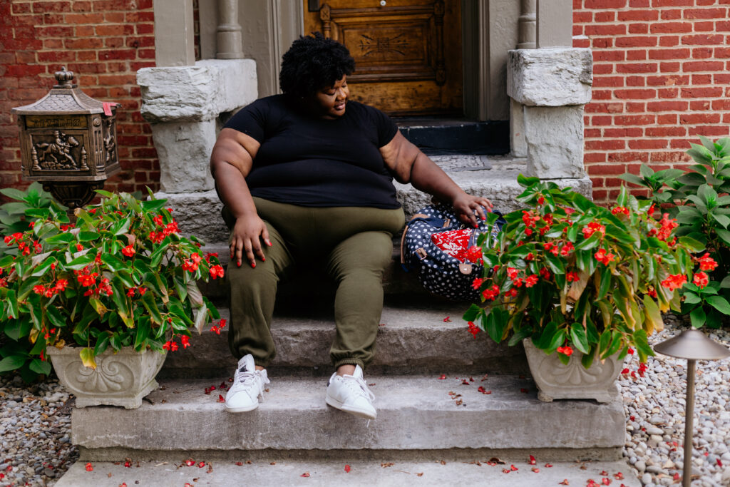 Kandice is sitting on front porch steps in her go to airport outfit.