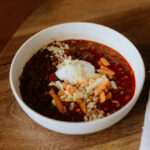 A bowl of beef and chorizo chili topped with shredded cheese and sour cream.