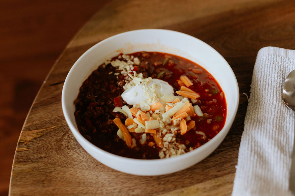 A bowl of beef and chorizo chili topped with shredded cheese and sour cream.