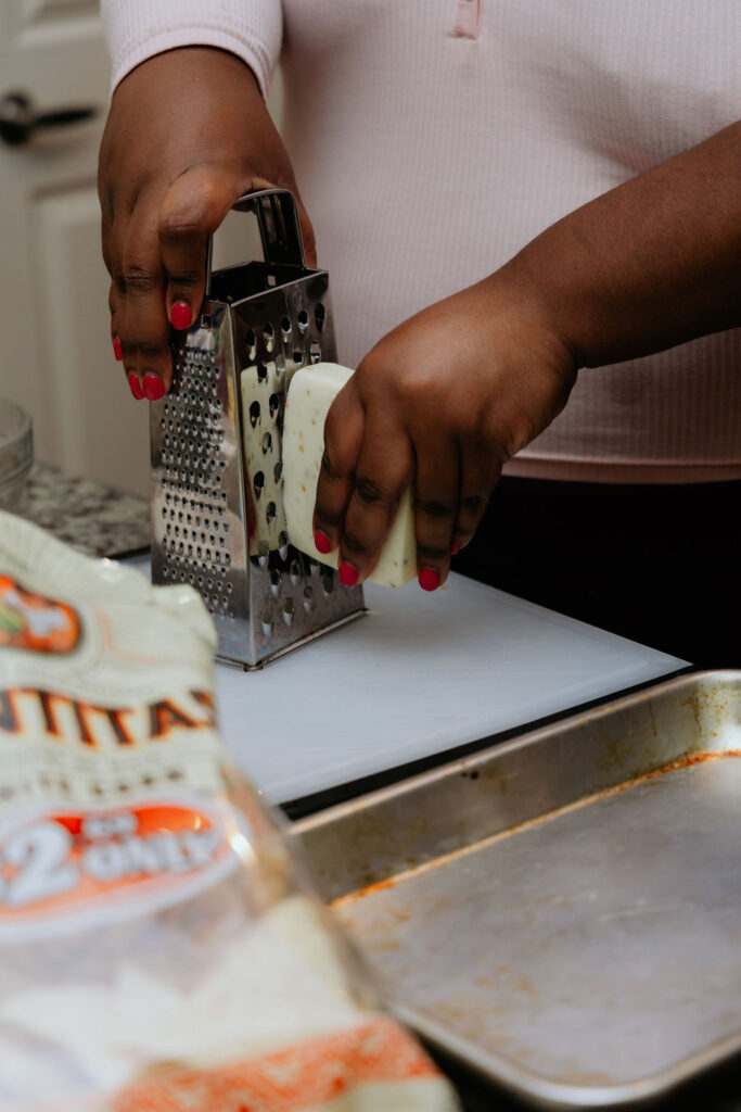 Kandice is grating cheese on a cutting board.