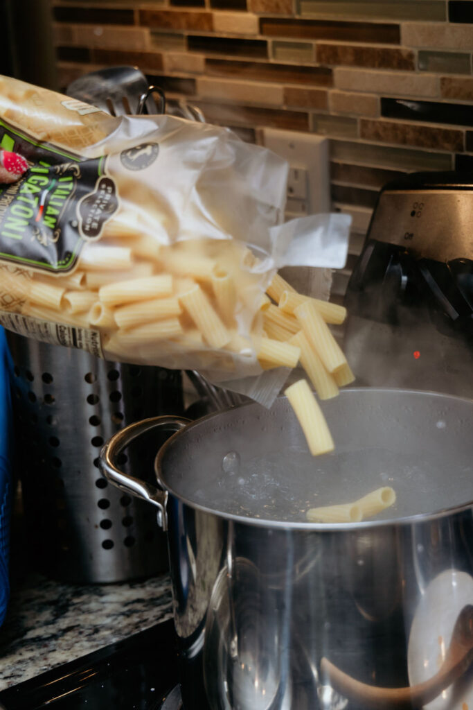 Kandice is pouring rigatoni into salted pasta water.