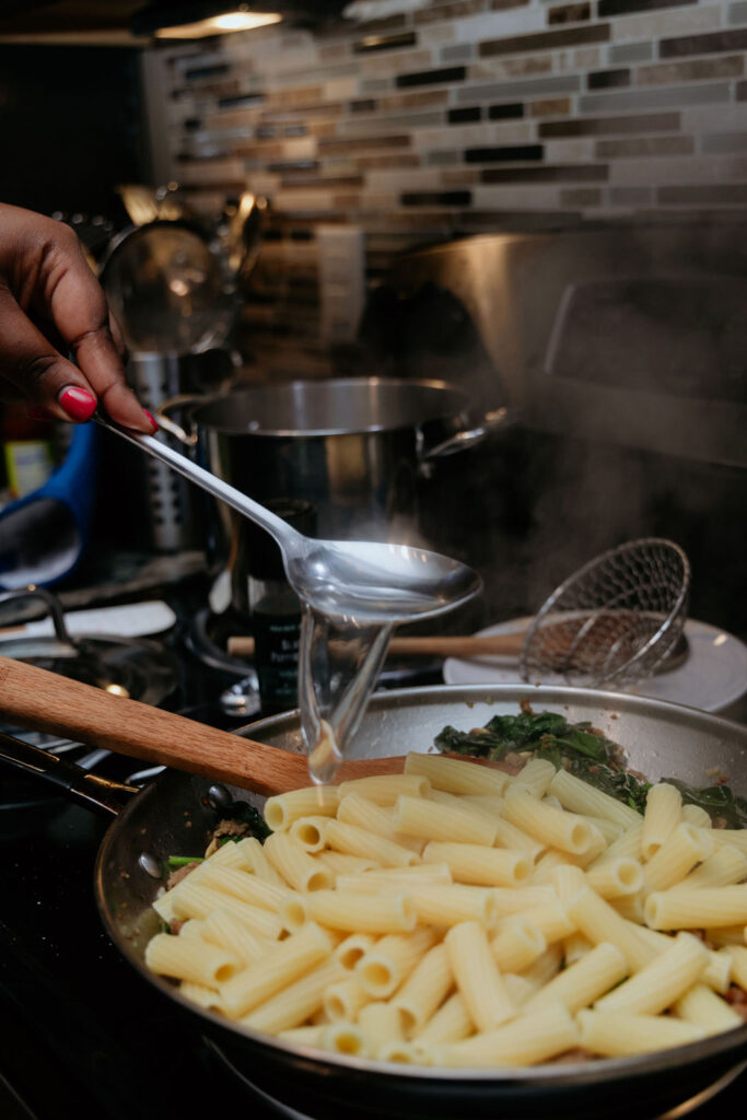 Kandice is adding starchy pasta water to skillet. 