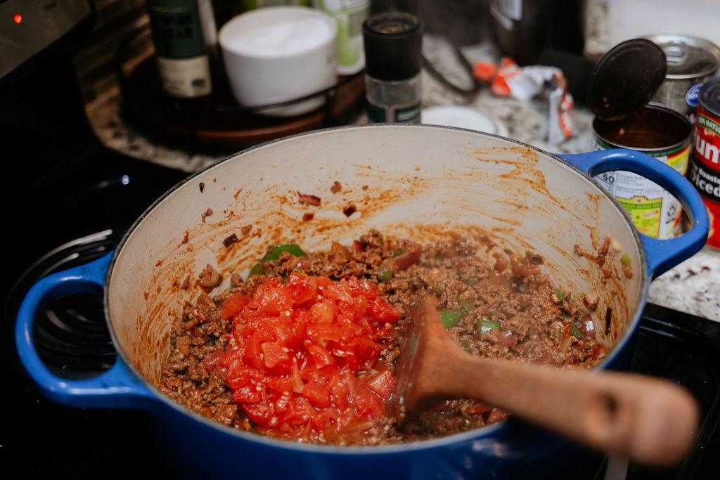 Kandice is adding tomatoes to chili.